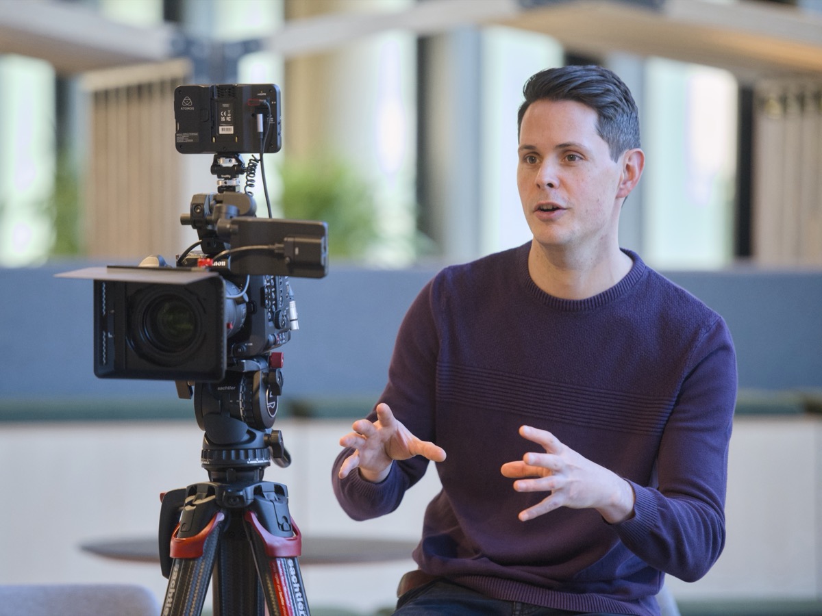 Joe from Cambridge TV talking on camera during an interview, the camera set up on its tripod beside him